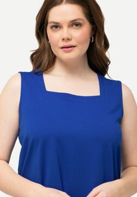 Top senza maniche blu con scollo quadrato, realizzato in tessuto morbido. Presenta una vestibilità ampia e un design semplice, adatto per un look casual.
