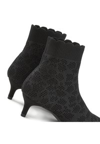 Botas negras hasta el tobillo con una textura de punto, cuello ondulado y un tacón bajo y cónico. Presenta un patrón de pequeñas formas elevadas en toda su superficie.