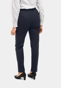 Marineblauwe op maat gemaakte broeken met een gladde textuur, elastische tailleband en taps toelopende pijpen. Gecombineerd met zwarte hoge hakken.