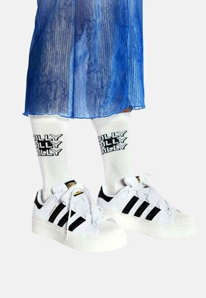White sneakers with black stripes and a rubber sole, paired with white socks featuring the text "DILLY DILLY" in bold black lettering.