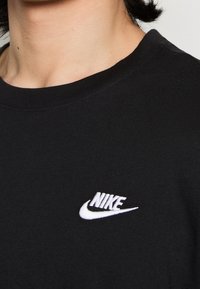 Černé bavlněné tričko s kulatým výstřihem, se bílou vyšívanou logem Nike na levé části hrudi. Měkká textura, casual design.