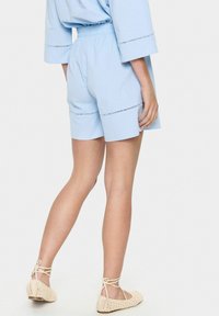 Gaiši zilie šorti ar elastīgu jostu un dekoratīvo šuvumu. Apvienoti ar bēšiem, austiem baleta zābakiem ar mežģīņu saitītēm.