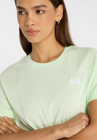 Camiseta corta de manga verde claro, fabricada en tejido suave, con un pequeño logo blanco de New Balance en el pecho.