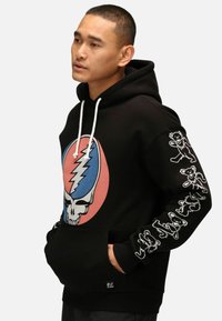 Felpa nera con un design grafico di teschio e fulmini in blu e rosa sul davanti; lacci bianchi e decorazioni di orsi colorati sulle maniche.