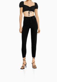 Top corto negro con mangas abullonadas, combinado con jeans skinny negros de cintura alta. La modelo lleva tacones negros con tiras.