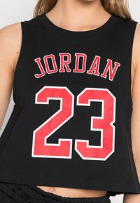 Musta puuvillainen lyhyt toppi, jossa on punaisella tekstillä nimi "JORDAN" ja sen alla numero "23" punaisella ja valkoisella ääriviivalla.