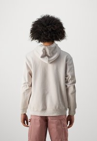 Hellgrau Kapuzenpullover mit langen Ärmeln und lockerer Passform, mit gerippten Bündchen und Saum. Getragen mit rosa Cargo-Hosen.