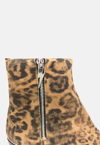 Botín de tobillo con estampado de leopardo, fabricado en ante, que presenta una cremallera lateral con un tirador en forma de rayo. Punta redonda y textura suave.