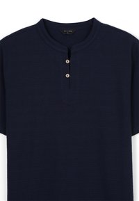 Maglietta a maniche corte blu navy con scollatura rotonda, dotata di una pattina con bottoni nella parte anteriore composta da due bottoni in legno chiaro e un tessuto testurizzato.