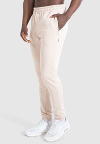 Helle beige Sweatpants aus weichem Stoff, mit einem elastischen Bund, seitlichen Taschen und schmal zulaufenden Beinen, kombiniert mit weißen Sneakers.
