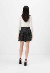 Black and white tweed skirt with fringe hem, paired with a fitted white long-sleeve top and black heeled sandals. Back view.
