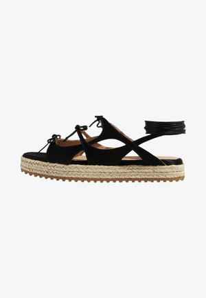 Zwarte suède espadrille sandaal met een gevlochten jute zool, voorzien van gekruiste banden, verstelbare enkelbanden en een platte rubberen zool.