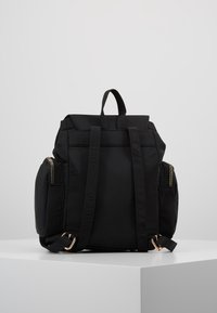 Czarny nylonowy plecak z górnym uchwytem, regulowanymi paskami, dwoma bocznymi kieszeniami na zamki oraz złotymi elementami ozdobnymi.