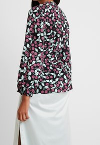 Blusa floreale con sfondo nero decorata da ciliegie rosa e foglie azzurre, maniche lunghe e dettagli arricciati sul retro.