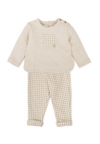 Top beis de manga larga con un bolsillo a cuadros y dos botones en el hombro. Pantalones de patrón a cuadros en beige y blanco a juego, con dobladillos acampanados.
