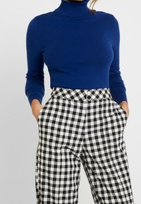 Niebieski sweter z golfem zestawiony z wysokim stanem czarno-białych spodni w kratę gingham, z bocznymi kieszeniami i luźnym krojem.