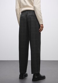 Pantalons à carreaux gris foncé avec une taille haute, un design à jambe droite, des poches latérales et une texture douce, associés à des bottes noires à la cheville.