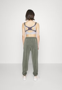 Reggiseno sportivo grigio e nero con design posteriore a taglio, abbinato a joggers verde oliva con vita elastica e orli risvoltati.