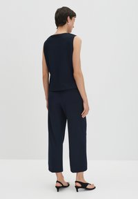 Navy sleeveless top and matching wide-leg pants in a smooth fabric, paired with black heeled sandals, viewed from the back.