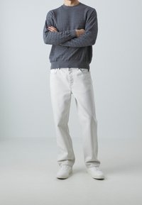 Szara teksturowana bluza z prążkowanymi mankietami i ściągaczem, zestawiona z białymi jeansami o prostych nogawkach i białymi trampkami. Prosty, nowoczesny design.