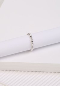 Silberner Ring mit einem Perlenmuster, der auf einem gerollten weißen Papier liegt, mit glatten Oberflächen und einem glänzenden Finish.