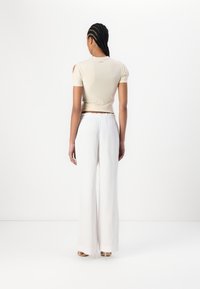 Top beige aderente con maniche corte e dettagli cut-out sulle spalle, abbinato a pantaloni bianchi a vita alta e a gamba larga realizzati in un tessuto leggero.