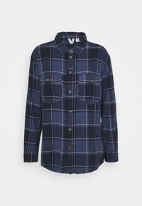 Camicetta di flanella blu navy con un motivo a quadri in azzurro chiaro e rosa. Presenta una chiusura con bottoni sul davanti e due tasche sul petto con pattina.