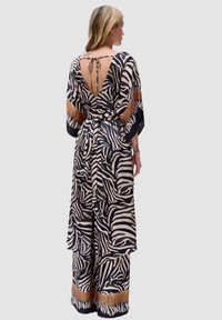 Zebra-geprint jumpsuit in beige en zwart, met een V-achterontwerp en een striksluiting, brede mouwen en een bruine accent bij de zoom.