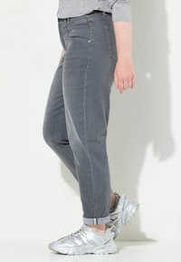 Jeans de mezclilla gris con corte recto, con bolsillos traseros y puños remangados, combinados con zapatillas deportivas metálicas plateadas.