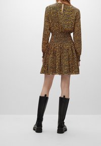 Zwarte jurk met gele luipaardprint, gerimpelde taille, ruches aan de onderrand, lange mouwen en een sleutelgat-detail aan de achterkant. Draag het met kniehoge zwarte laarzen.