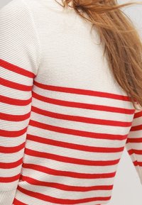 Pull-over en maille présentant des rayures horizontales alternées rouges et blanches, avec un tissu texturé et un design d'encolure simple.