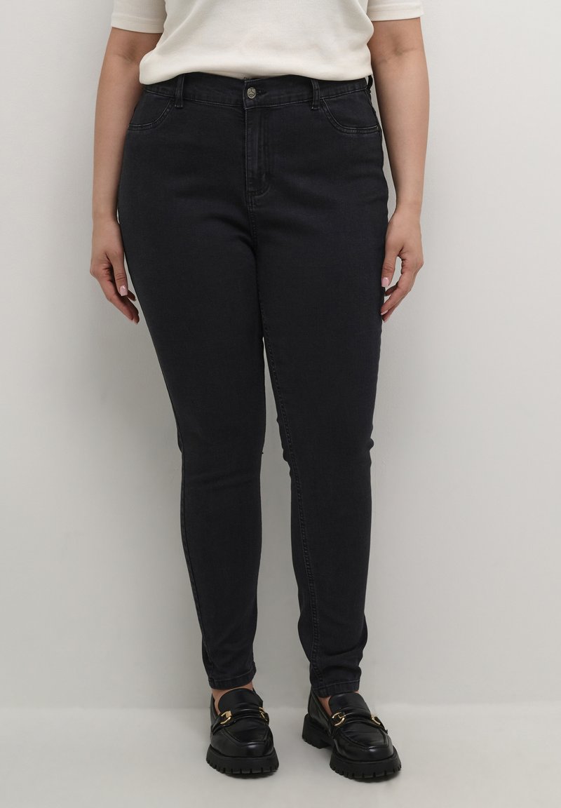 Jean skinny bleu foncé avec une taille mi-haute, cinq poches et un tissu en denim lisse et légèrement texturé. Fini avec une fermeture à bouton.