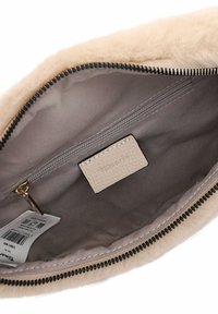 Pochette en fausse fourrure de couleur beige clair avec un intérieur lisse. Équipée d'une fermeture éclair foncée et d'une étiquette texturée avec "Tamara" embossé.