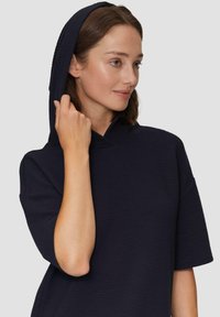 Granatowa bluza z kapturem, wykonana z teksturowanej dzianiny prążkowanej i z krótkimi rękawami. Posiada wysoki kołnierz oraz luźny fason.