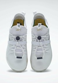 Paire de chaussures de sport blanches avec lacets élastiques, sangles ajustables, et semelles intérieures à motif jaune vues de dessus.