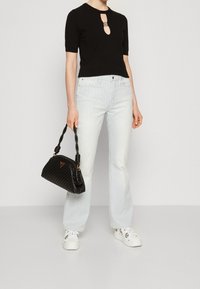 Top negro de manga corta con detalle de ojal, jeans de pierna ancha a rayas azul y blanca, zapatillas blancas y un bolso de mano negro tejido con logo.