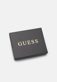 Scatola regalo nera con il logo dorato "GUESS" centrato sul coperchio. Texture liscia, forma rettangolare e angoli leggermente arrotondati.