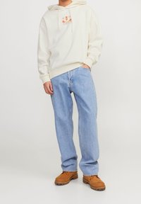 Krämfärgad hoodie med frontgrafik, parat med ljusblå vida jeans och bruna mockaskor. Hoodien har snoddar och ribbad nederkant.