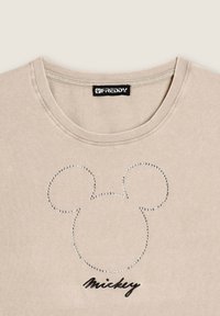 Camiseta beige de la marca Freddy con un contorno de strass de la cabeza de Mickey Mouse y el texto negro "Mickey" debajo del diseño.