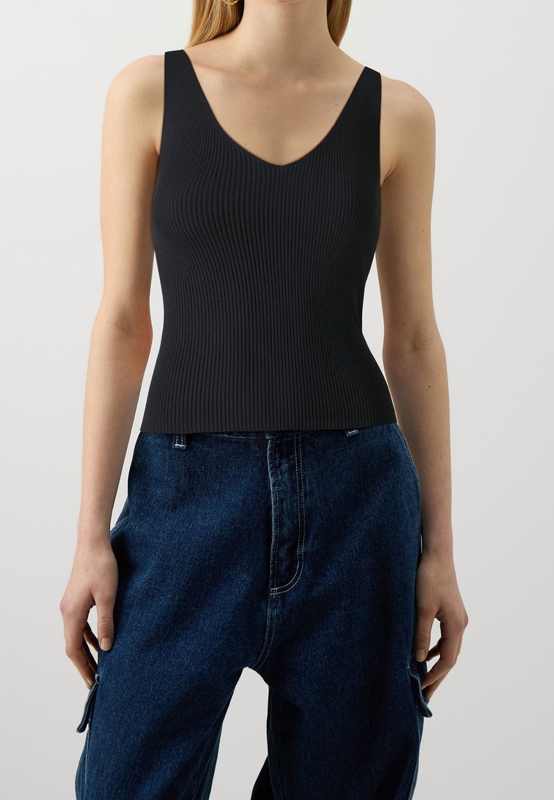 Camiseta negra acanalada sin mangas con escote en V y tirantes anchos, diseño ajustado, combinada con jeans de mezclilla oscuros de talle alto. Detalle sutil de textura.