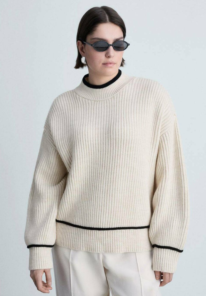 Cremefarbener gerippter Strickpullover mit schwarzem Besatz an den Bündchen und dem Saum, ausgestattet mit einem hohen Kragen und einem lässigen Schnitt, kombiniert mit dunklen Sonnenbrillen.