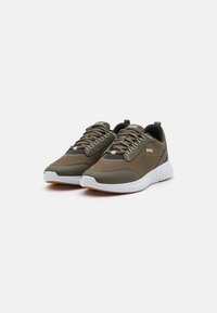 Tumši zaļi sneakers ar acu audumu augšdaļu, baltu vidējo zoli un brūnu gumijas zoli. Iespējas plakanās šņores un logo uz sāna.