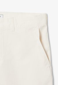 Pantaloni in cotone beige con una texture liscia, dotati di una vita standard e tasche laterali. Design semplice, senza motivi o hardware visibili.