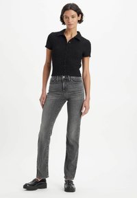 Black textured short-sleeve shirt with a collar, button front, paired with high-waisted, straight-leg gray jeans and black chunky shoes.