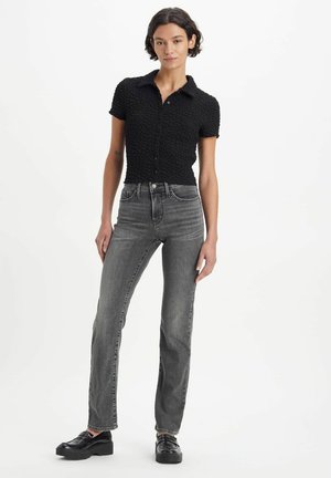 Schwarzes, strukturiertes Kurzarmhemd mit Kragen und Knopfleiste, kombiniert mit hochgeschnittenen, geraden grauen Jeans und schwarzen klobigen Schuhen.