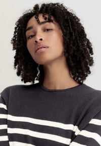 Marineblauer Pullover mit weißen horizontalen Streifen, Rundhalsausschnitt, strukturiertem Strickstoff und kurzen Ärmeln. Nahaufnahme des Oberkörpers.