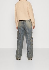 Afskåret beige fleecejakke med krave, parret med løse blå denim cargo bukser med sidelommer og en falmet finish.