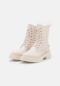 Botas de tobillo de color beige claro, hechas de cuero, con detalles trenzados, ojales dorados y suelas de goma gruesas con un acabado texturizado.