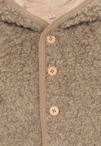 Zacht beige babycardigan met houten knopen, textuurwol en een geribbeld randje rond de kraag en knopenrij, maat 6 maanden.