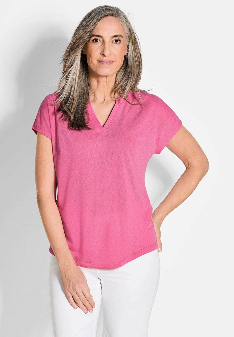Rosa Kurzarmoberteil mit V-Ausschnitt, aus weichem Stoff. Glatte Textur und lässige Passform, kombiniert mit weißen Hosen.